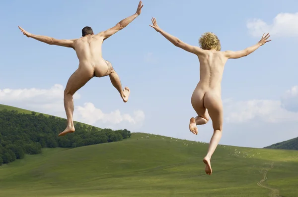 Naked couple jumping in field — Stock Photo, Image